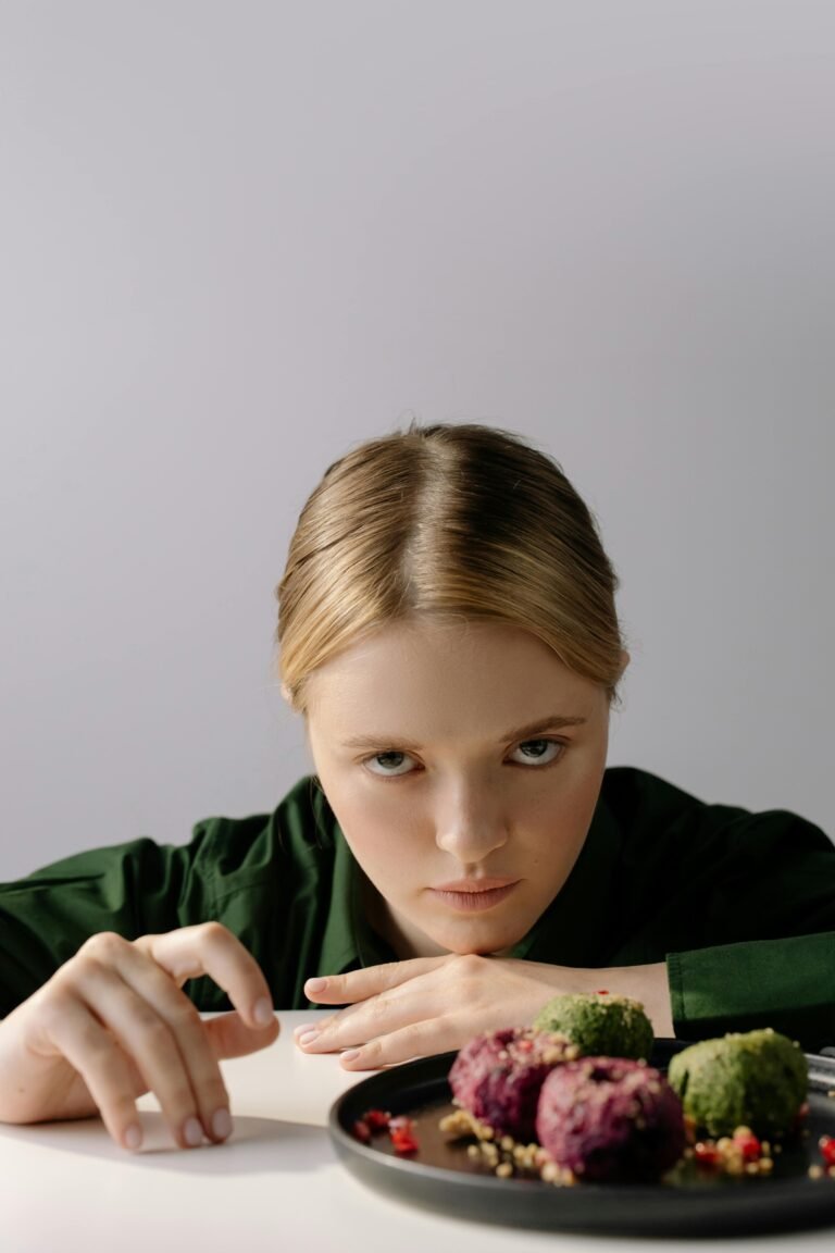 Blonde woman in green shirt with Georgian pkhali dish on table. Studio portrait with traditional food.