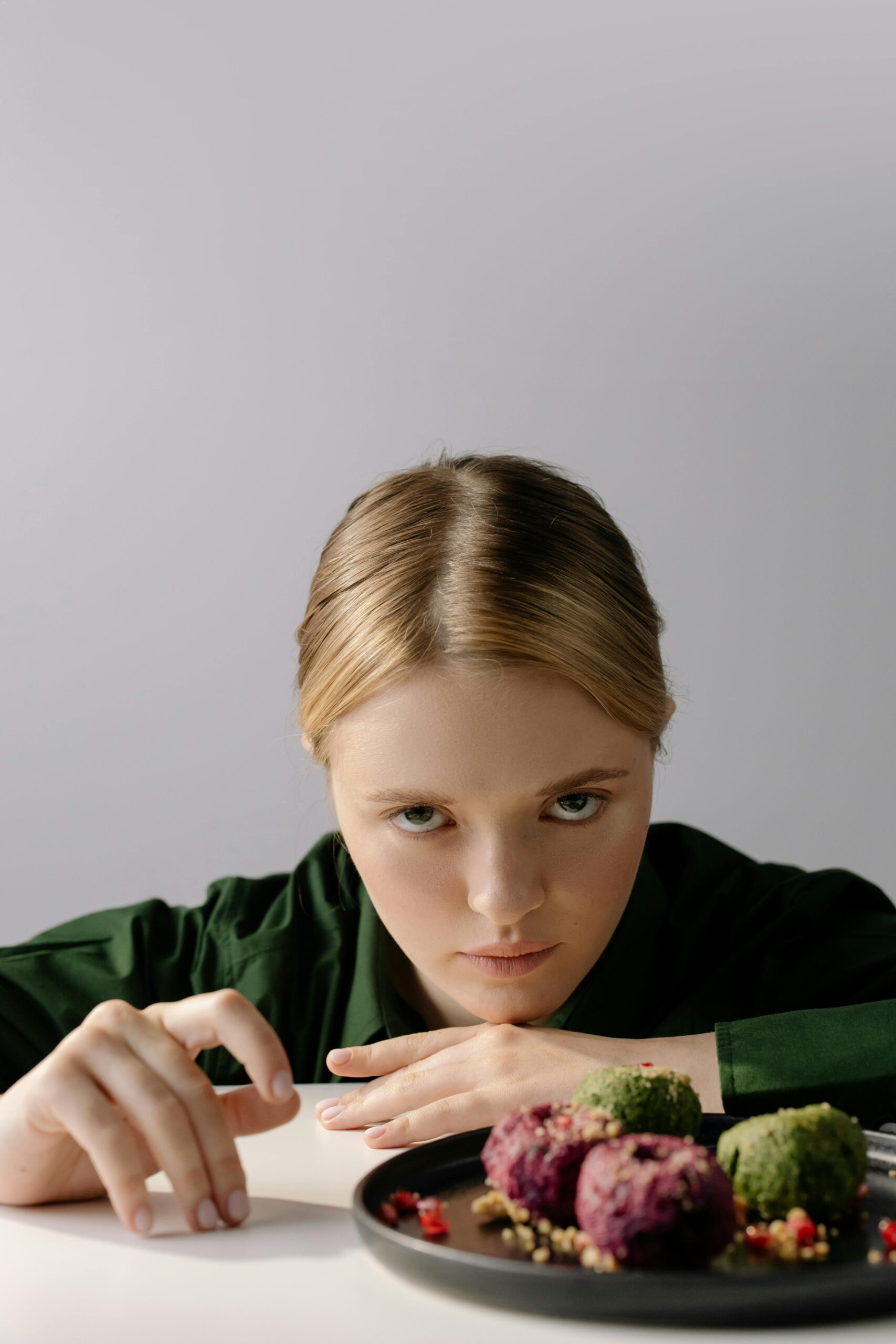 Blonde woman in green shirt with Georgian pkhali dish on table. Studio portrait with traditional food.