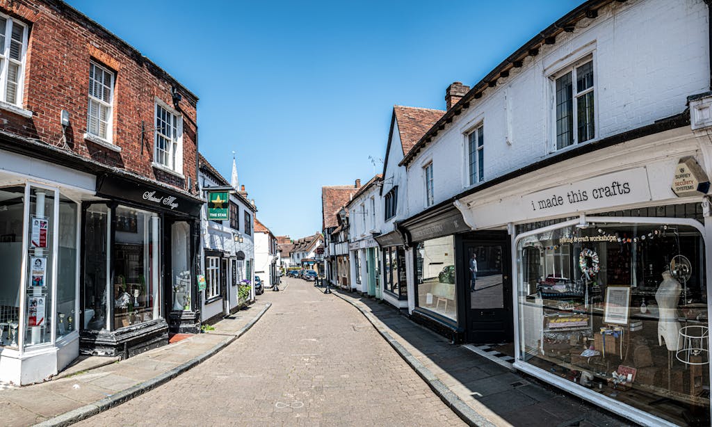 Picturesque view of an empty street in historic Godalming, England with old shops and blue sky.