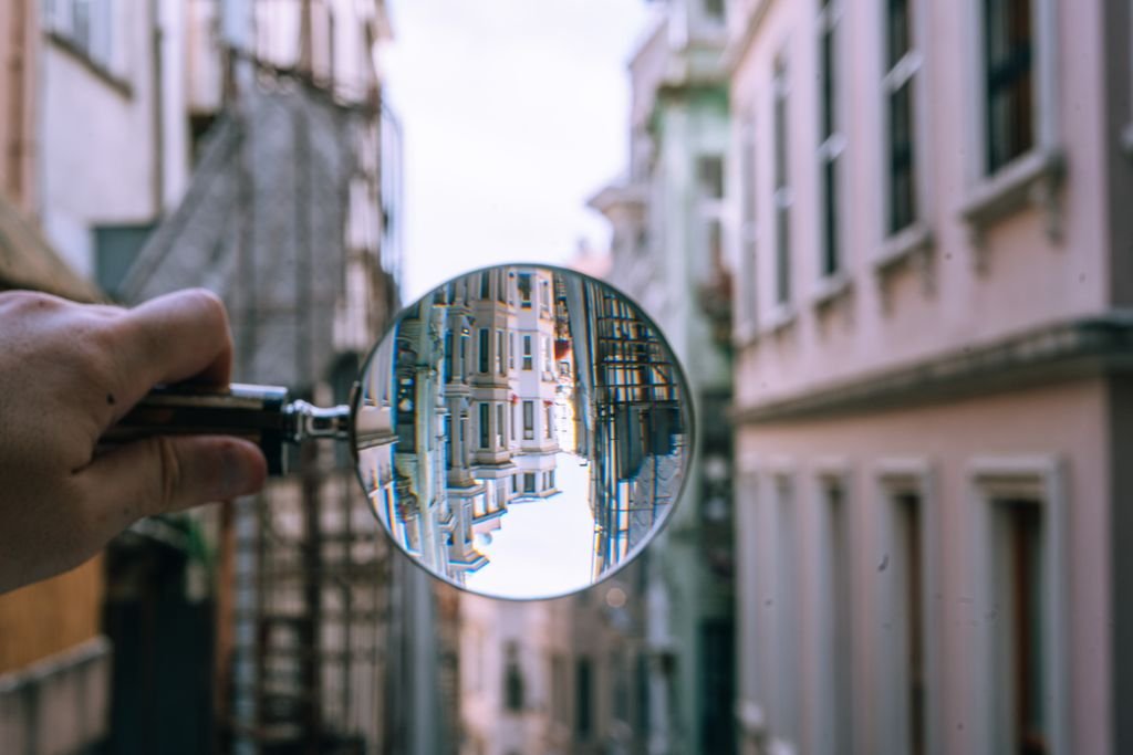 A hand holding a magnifying glass reflecting an upside-down cityscape with blurred buildings.