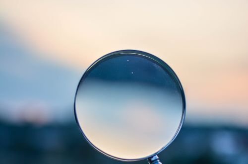A magnifying glass held by a hand outdoors at sunset, focusing on exploration.