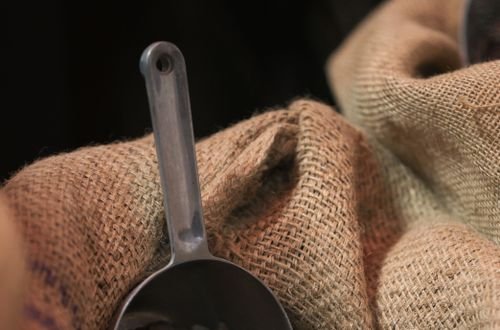 Chocolate bar in scoop on cocoa beans in burlap sack, showcasing premium chocolate production.