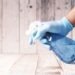 A gloved hand holding a blue spray bottle against a wooden background.