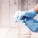 A gloved hand holding a blue spray bottle against a wooden background.