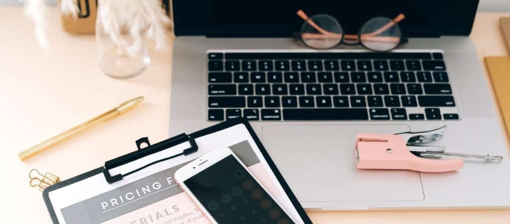 A stylish workspace featuring a laptop, smartphone, clipboard, and stationery essentials.
