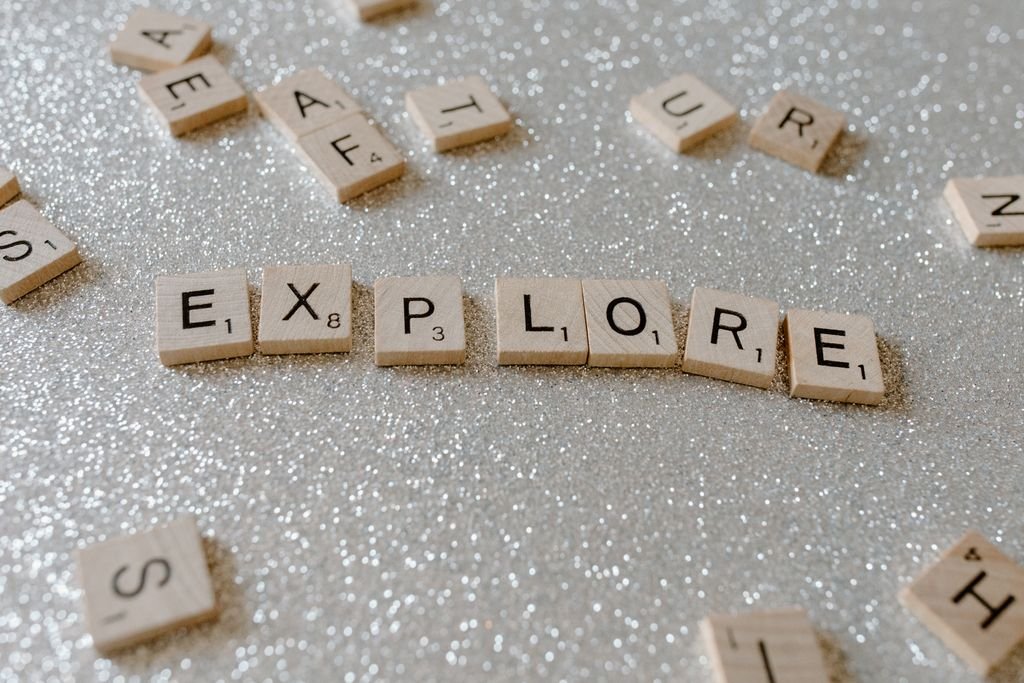 Close-up of wooden letter tiles spelling 'explore' on a sparkling gray surface.