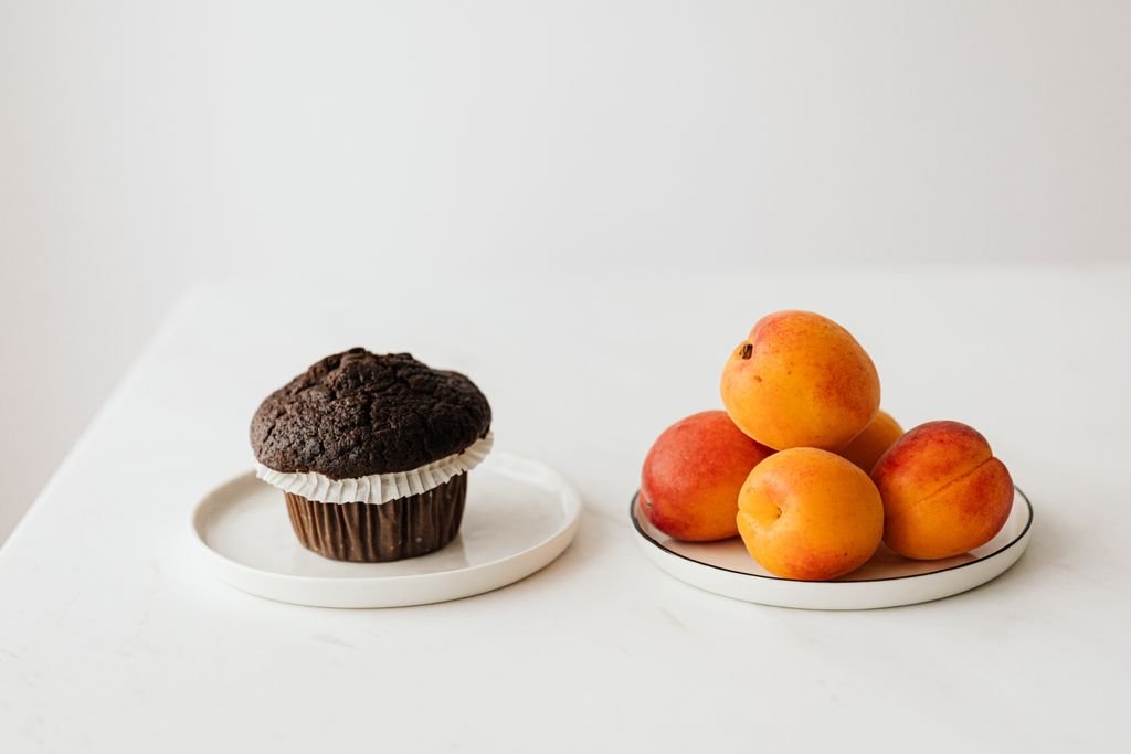 High angle of sweet chocolate cupcake composed with fresh natural ripe apricots against white background