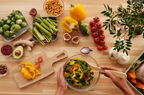 Top view of fresh vegetables and salad preparation on a wooden table, perfect for healthy eating concepts.