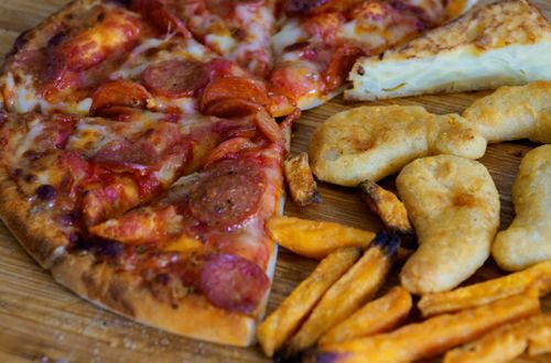 A close-up shot of pizza, Spanish omelette, sweet potato fries, and nuggets on a wooden table.
