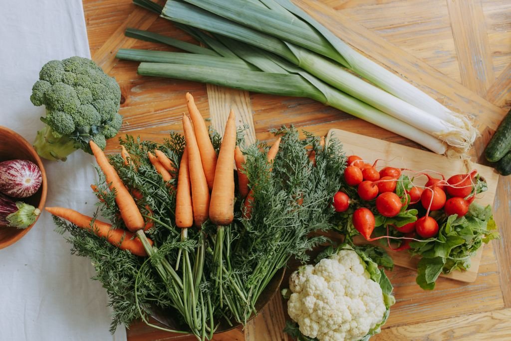 A colorful assortment of fresh vegetables including food carrots, leeks, and radishes displayed on a wooden table.