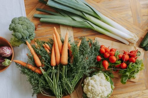 A colorful assortment of fresh vegetables including carrots, leeks, and radishes displayed on a wooden table.