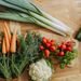 A colorful assortment of fresh vegetables including carrots, leeks, and radishes displayed on a wooden table.