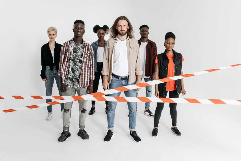 A diverse group of serious individuals lined up behind caution tape against a white background.