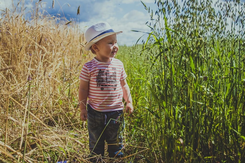 A happy child wearing a straw hat enjoying a sunny day in a green field, surrounded by nature.