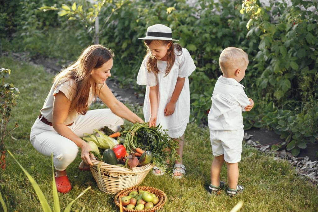 A mother and her children picking fresh food vegetables in a sunny garden.
