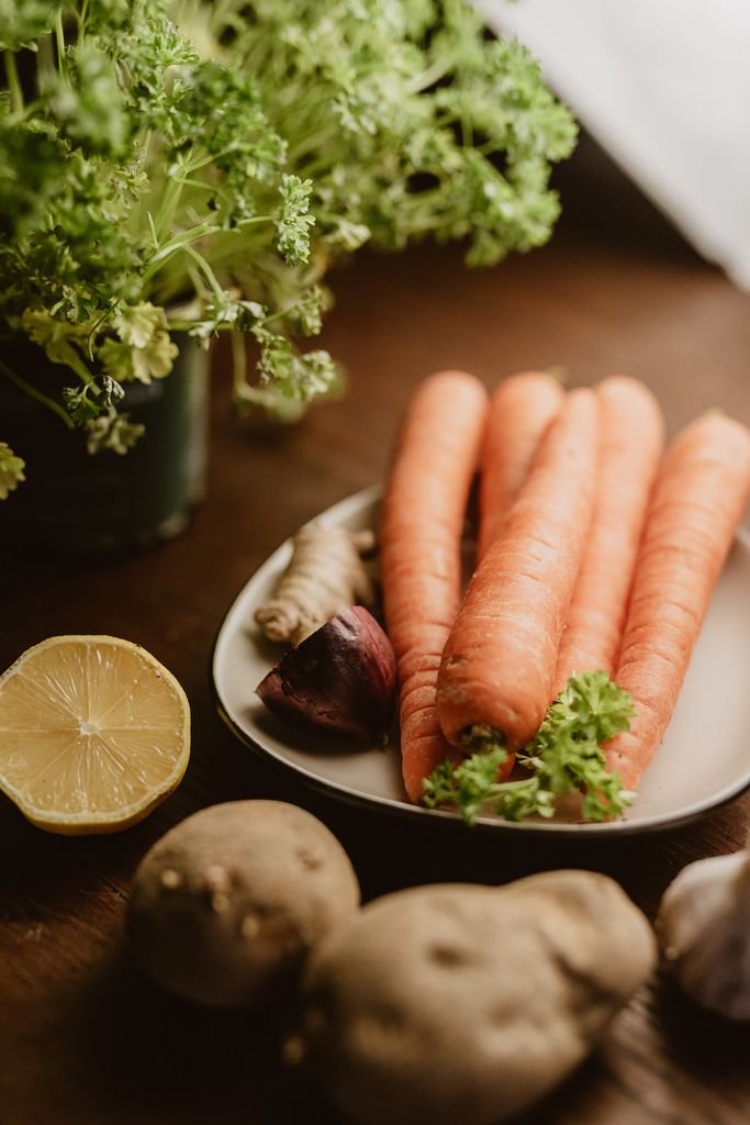 A rustic display of fresh carrots, herbs, and vegetables on a wooden table, perfect for culinary themes.