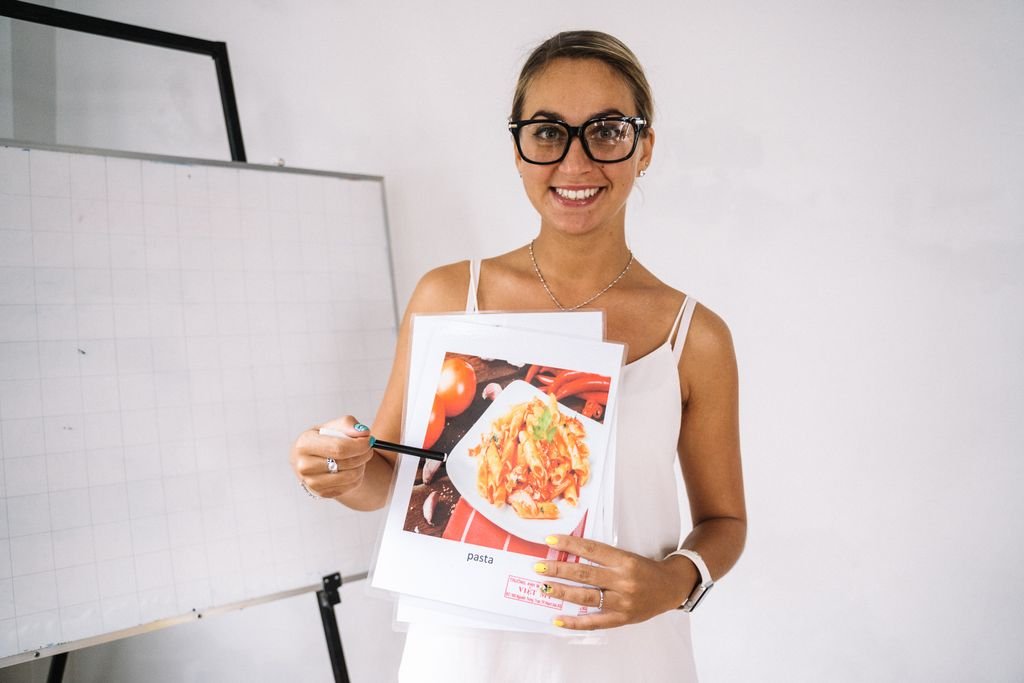 A teacher in a classroom holding a food illustration, highlighting culinary education.