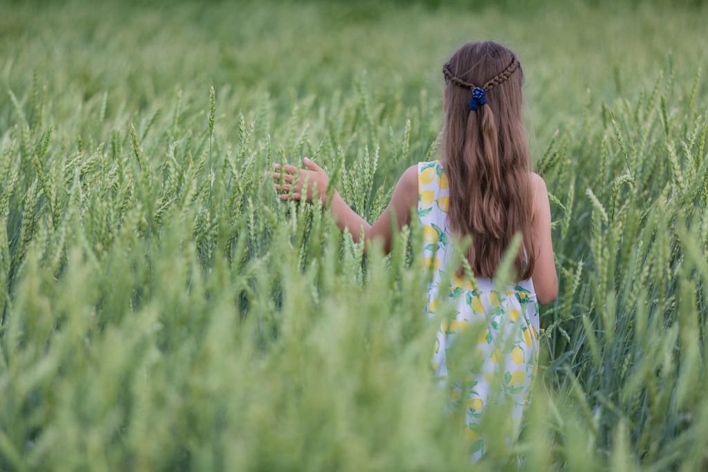 A young girl walks through a lush green wheat field, enjoying a summer day.