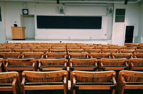 An empty lecture hall featuring wooden chairs and a large blackboard.