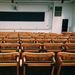 An empty lecture hall featuring wooden chairs and a large blackboard.