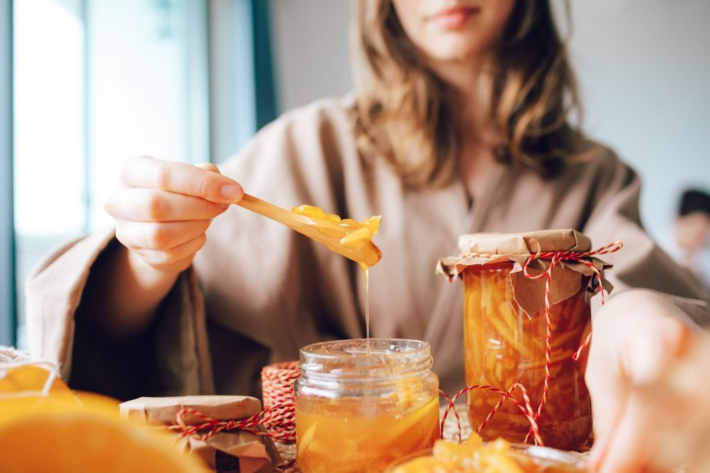 Close-up of a woman preparing fresh orange marmalade in glass jars, capturing the essence of homemade cuisine. food