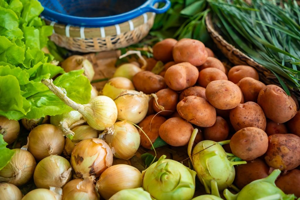 Close-up of assorted fresh vegetables including onions, potatoes, and greens at a farmers market stall. food