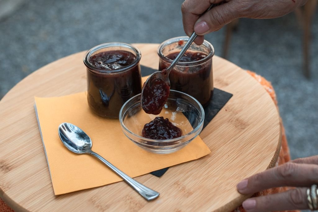 Close-up of hands transferring homemade jam from jars to a bowl on a wooden table. food