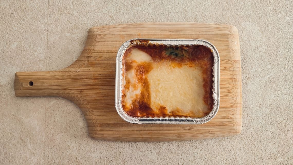 Delicious cheesy lasagna in an aluminum tray served on a wooden board.