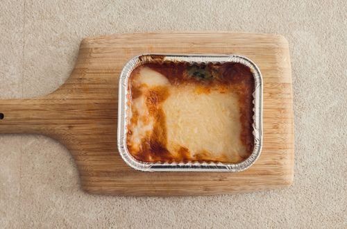 Delicious cheesy lasagna in an aluminum tray served on a wooden board.