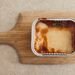 Delicious cheesy lasagna in an aluminum tray served on a wooden board.