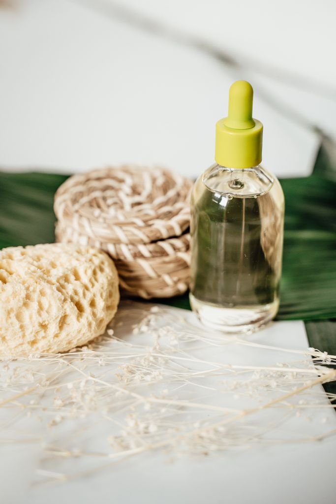 Eco-friendly skincare product with dropper bottle, sponge, and rope on a green leaf.