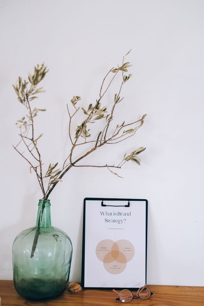 Elegant still life of a green vase with branches beside a clipboard and eyeglasses, epitomizing minimal design.