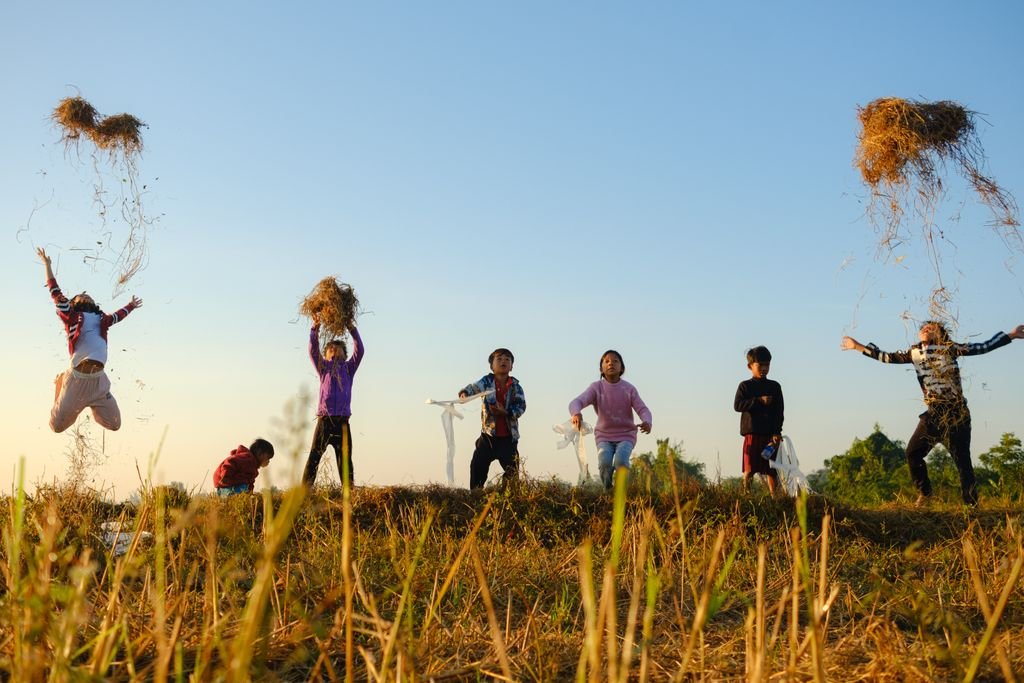 Joyful children tossing hay in a sunny Battambang field, Cambodia.