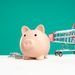 Piggy bank with shopping cart and coins on a white and teal background, symbolizing saving and spending.