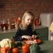 Positive little girl and boy sitting at desk with various fresh vegetables and fruits while preparing meal in loft kitchen with brick wall