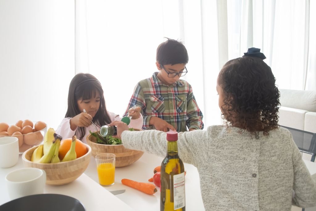 Three children making a fresh salad together in a modern, bright kitchen setting.
