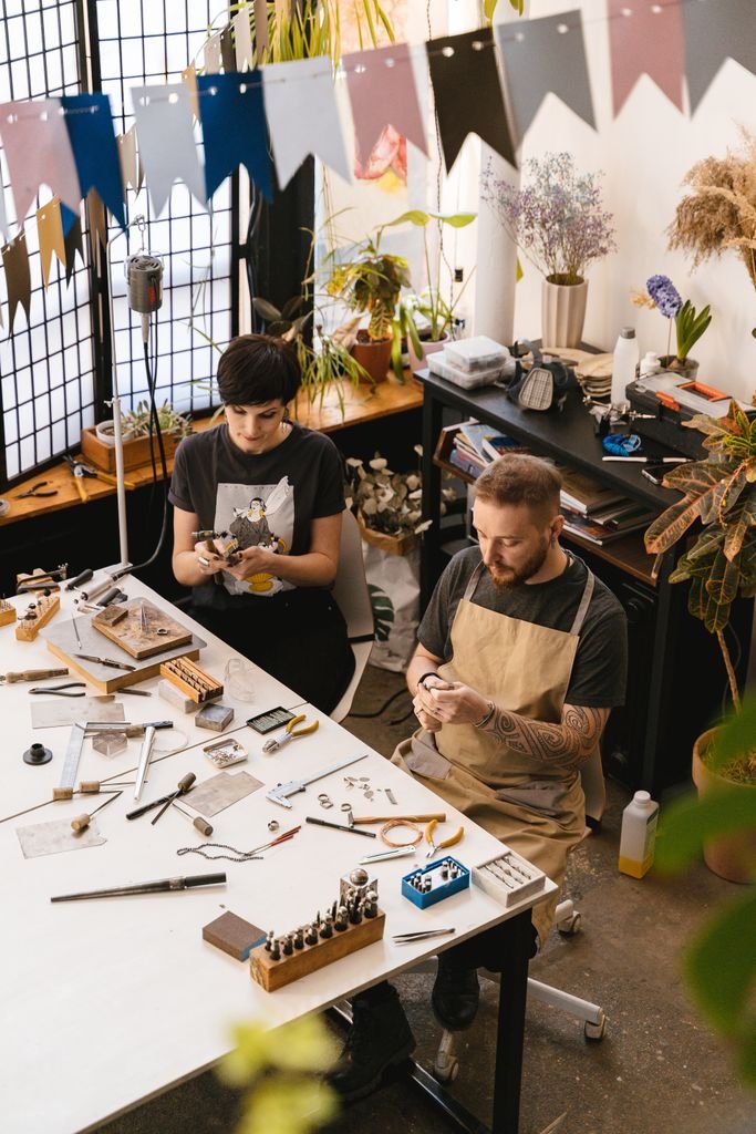 Two artisans working on handmade jewelry in a creative workshop setting.