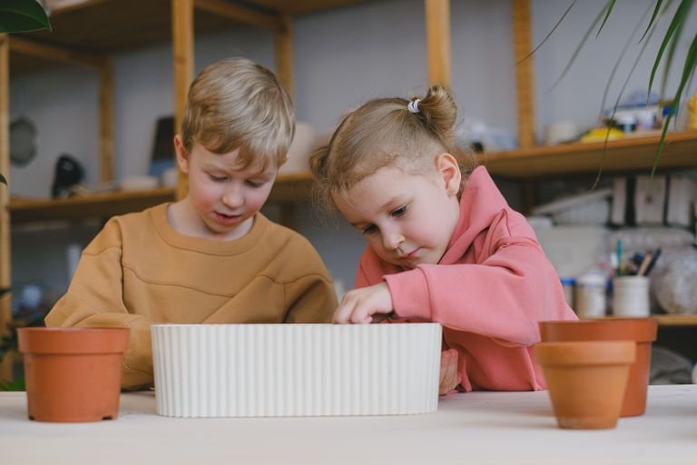 Two children engaged in an indoor gardening project, planting in pots.