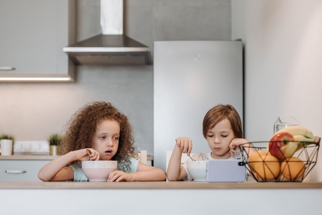 Two children having breakfast together at home, enjoying a meal at a clean, modern kitchen counter.