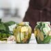 Two glass jars filled with homemade pickled cucumbers and herbs on a white kitchen surface.