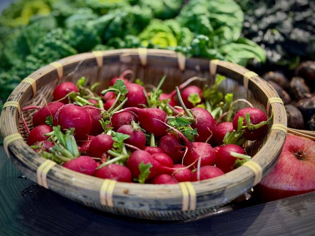 Vibrant red radishes food in a rustic bamboo basket surrounded by leafy greens, conveying a fresh farm-to-table feel.