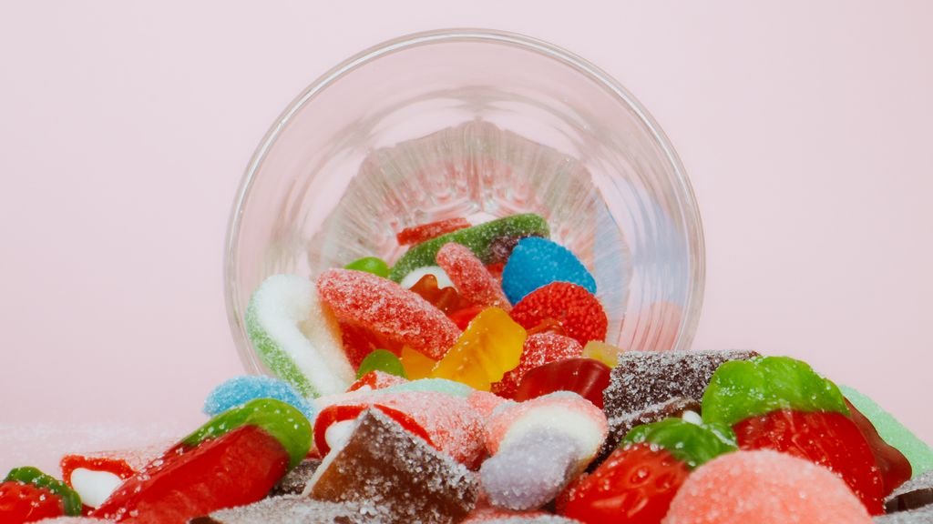 Vibrant sweet gummies food spilling from a bowl on a pastel background.