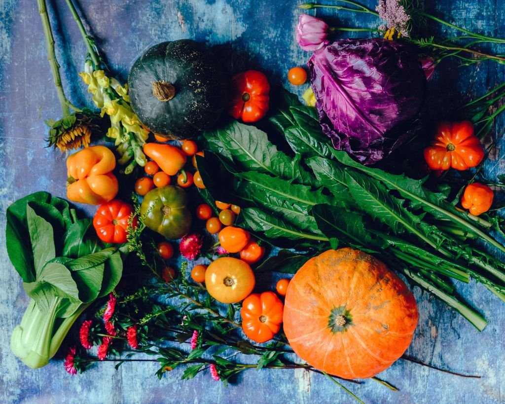 A vibrant assortment of fresh vegetables including pumpkins, cabbage, and tomatoes on a rustic surface. seasonal produce