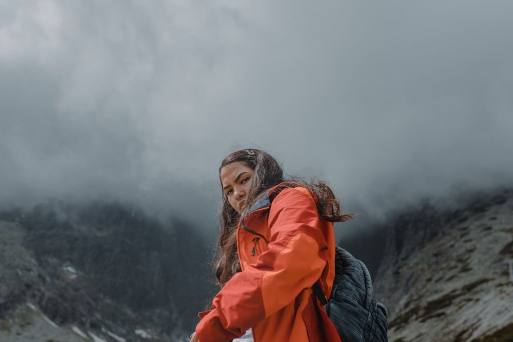 A woman in an orange jacket hiking on a foggy mountain day.