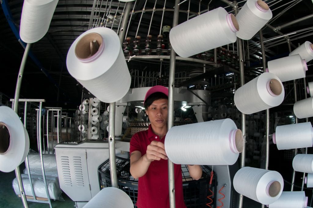 Industrial worker managing yarn spools on a textile machine in a factory. nylon